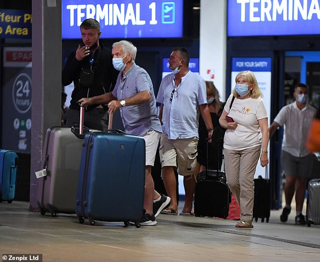 一群人站在商店前：此后度假者一直在支付高昂的费用，以避免如果未接种疫苗，返回后会被隔离十天。 图为：乘坐截止日期前最后一班航班从伊维萨岛抵达曼彻斯特机场的乘客